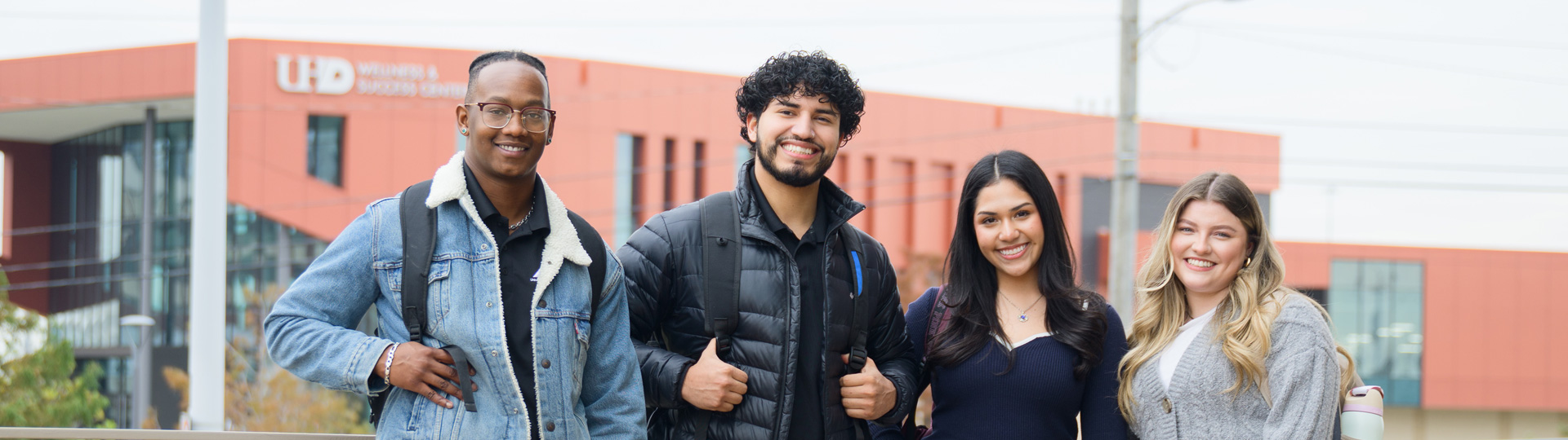 Four UHD students smiling at the camera with the Sciences and Technology building as a background