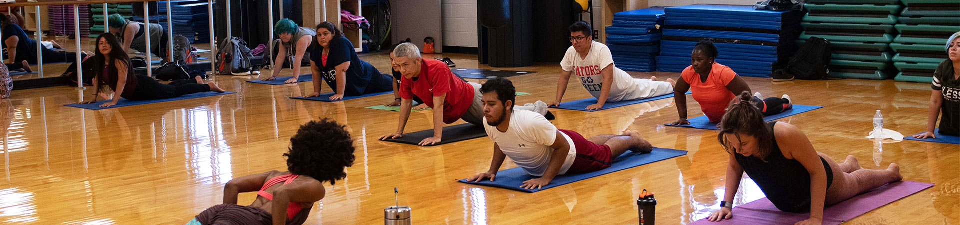 UHD students on mats on the floor of the gym in yoga poses