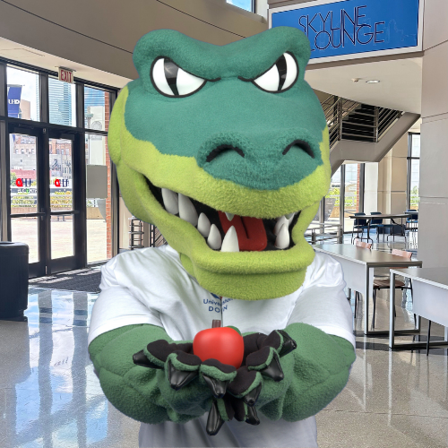 UHD mascot Ed-U-Gator holds an apple in the university's Skyline Lounge 