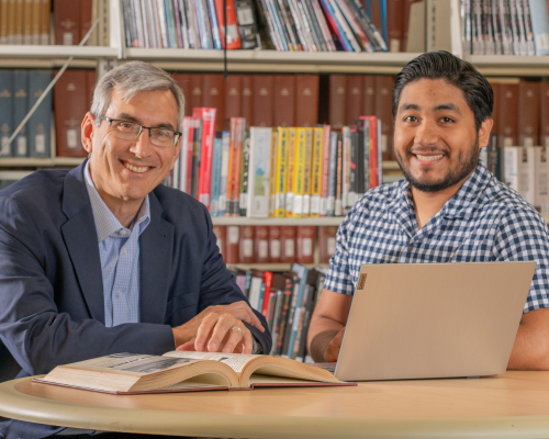 Dean Kostantaras, Honors Program Director at University of Houston Downtown, sits aside an open book, laptop, and University of Houston Downtown alum Iker Pelcastre
