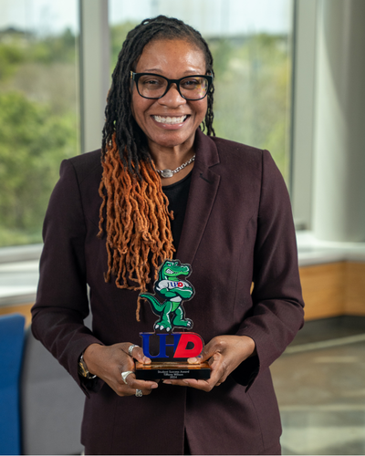 Tiffany Wilson University of Houston-Downtown Counselor holds the 2024 Student Success Staff Award while smiling in the university's Welcome Center