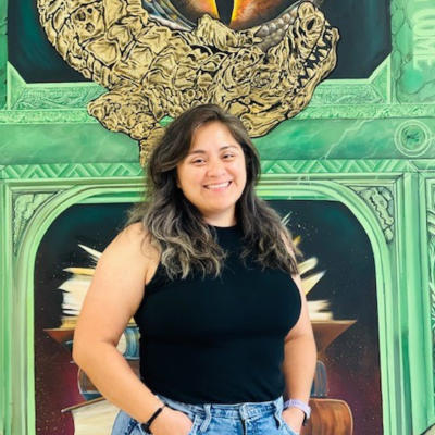 Director of College of Humanities and Social Sciences Advising Center Vanessa Rojas smiles in front of the college's Gator mural