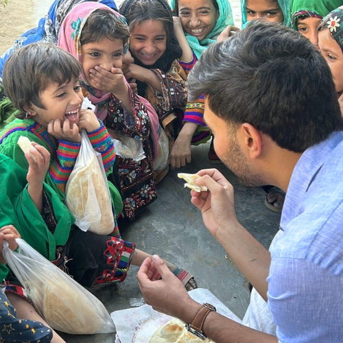 Ammar Ansari Psychology major and senior at the university of houston-downtown holds a piece of flat bread while children laugh and smile around him 