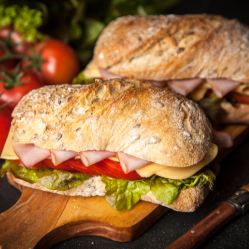two sandwiches with sliced deli meat, cheese, and lettuce on a serving board 