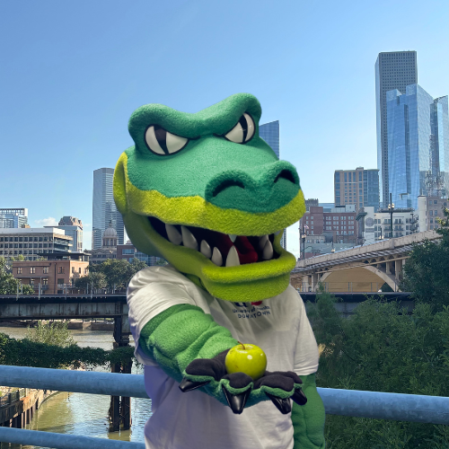 ed u gator holds a green apple on a walking bridge on the university of houston downtown campus