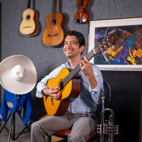 David Moreno, Mariachi Director at the University of Houston-Downtown, plays a guitar and smiles. 