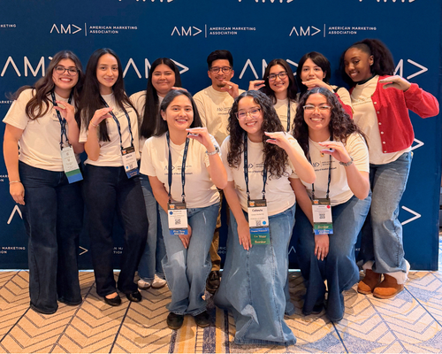 Ten members of the american marketing association at the university of houston-downtown make gator hand signs in front of an american marketing association step and repeat at the 2026 american marketing association international collegiate conference in chicago