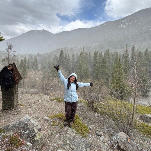 Senior at the University of Houston-Downtown Kayla Palucho raises her arms while it is snowing. Mountains are behind the student. 