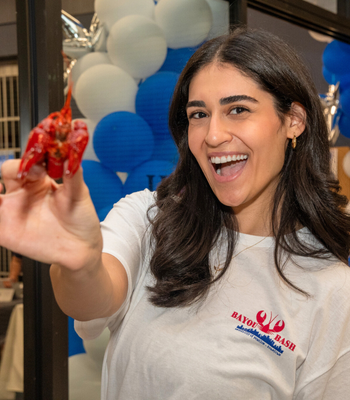 An adult holds up a crawfish and wears a University of Houston-Downtown Bayou Bash t-shirt at the university's annual crawfish boil and celebration Bayou Bash